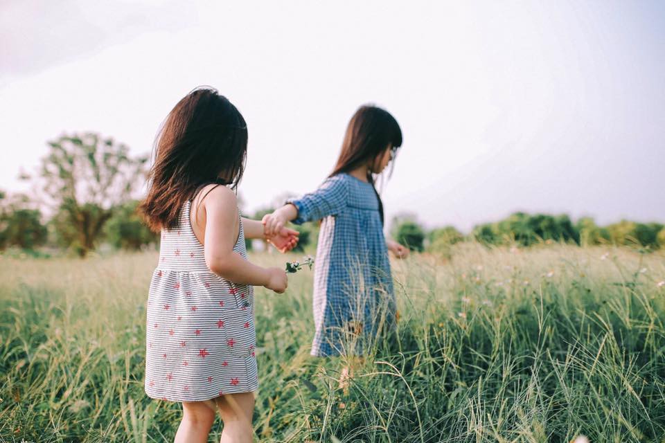 Ảnh 2 cô bé đang dắt tay đi trên đồng cỏ bát ngát rất thân thiết. 